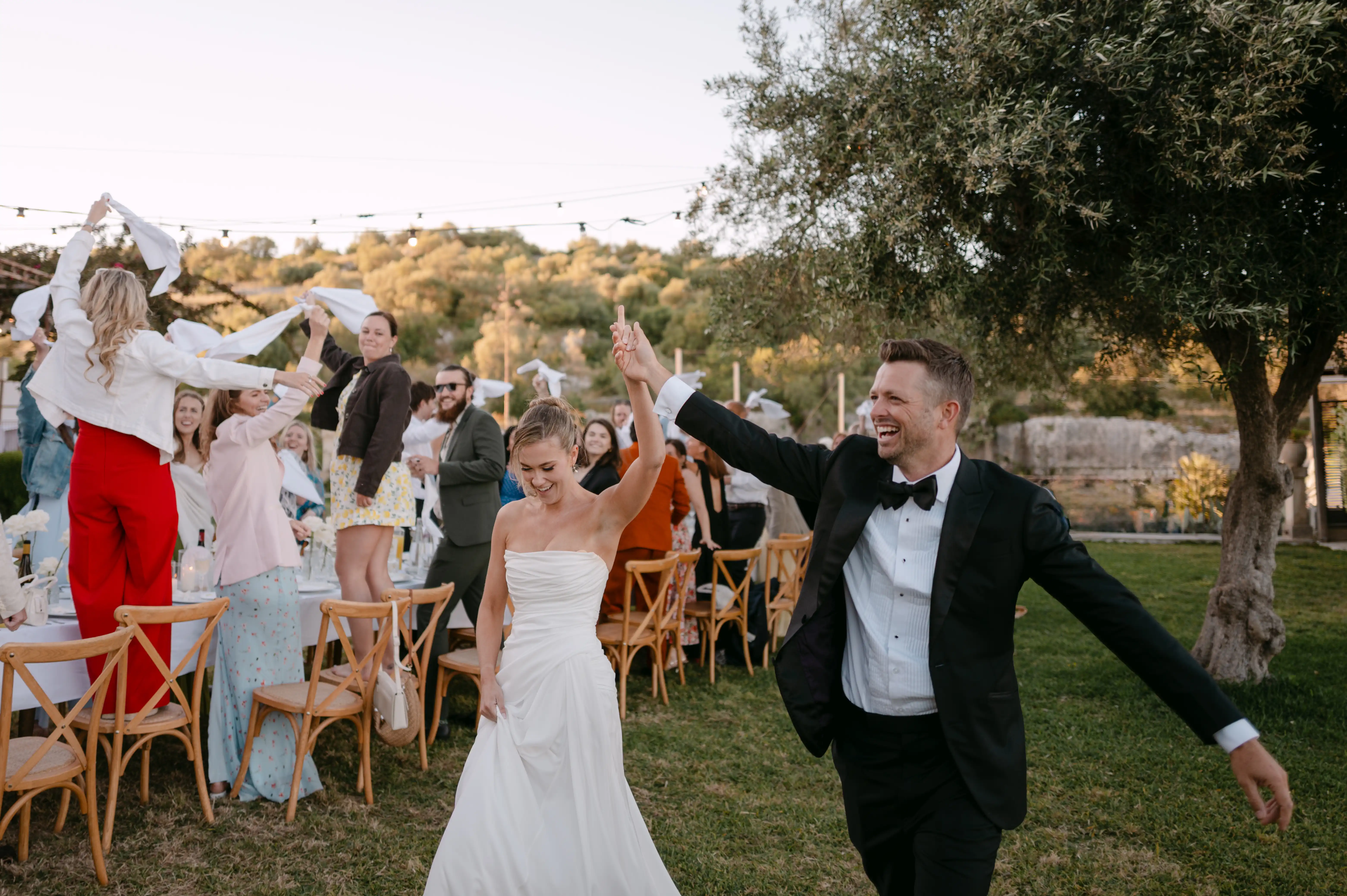 Newlywed couple celebrating with guests during a lively outdoor wedding reception in the Italian countryside.